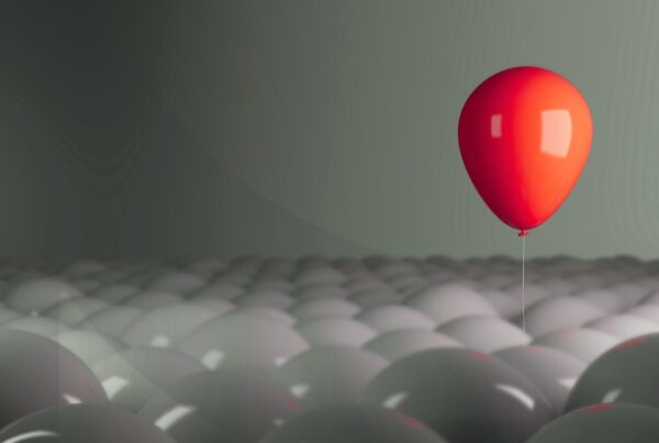Red balloon floating above a large group of gray balloons.