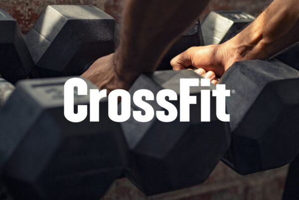 Athlete gripping hex dumbbells during strength training workout at gym with Crossfit logo on top of image