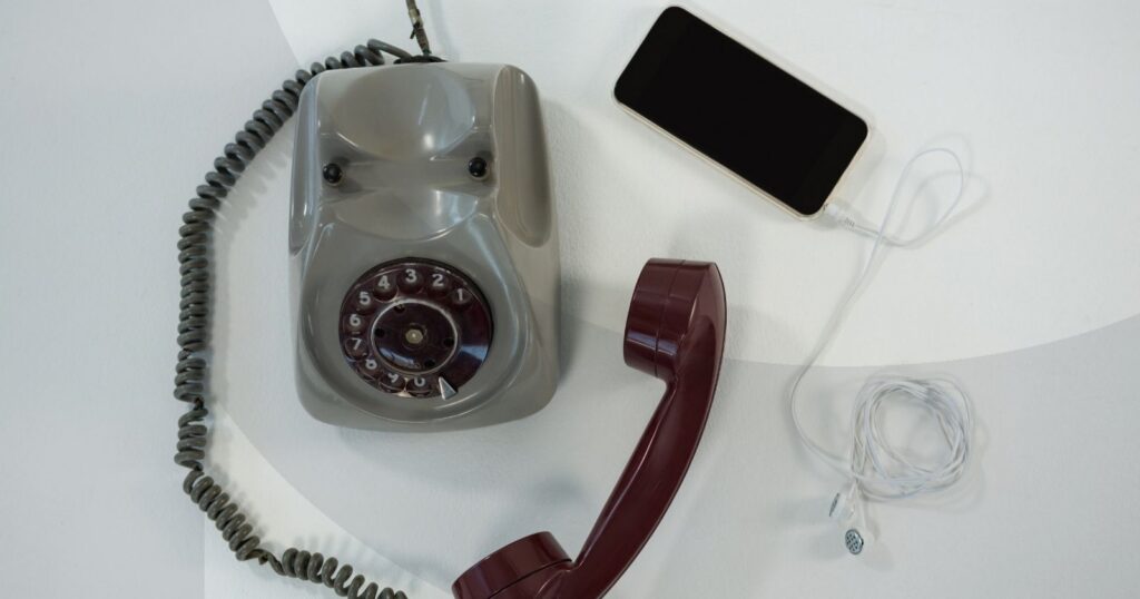 A wired rotary telephone laying next to a smartphone with wired earbuds plugged into it.