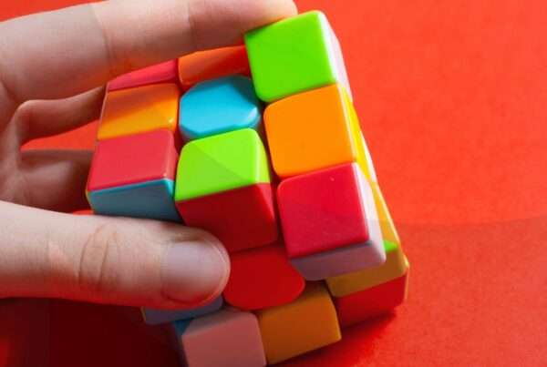 A hand solving a rubik's cube against an orange background.