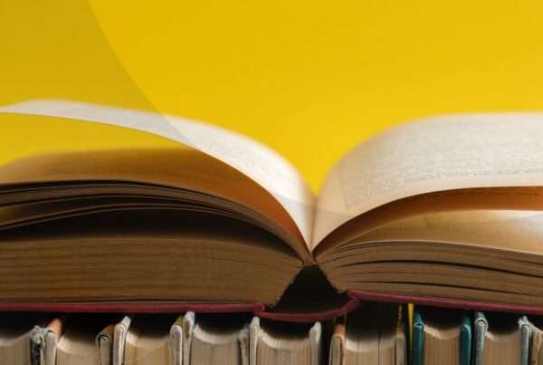 An open hardcover book resting on top of other hardcover books against a yellow background.