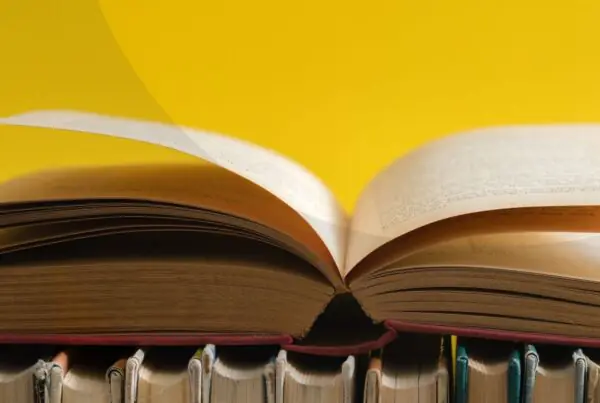 An open hardcover book resting on top of other hardcover books against a yellow background.