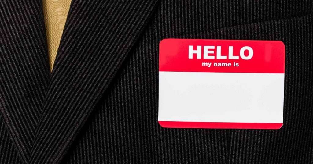 A blank, red, and white nametag sticker on the breast of a black pinstripe suit with a golden tie.