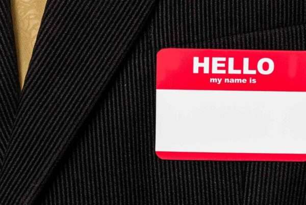 A blank, red, and white nametag sticker on the breast of a black pinstripe suit with a golden tie.