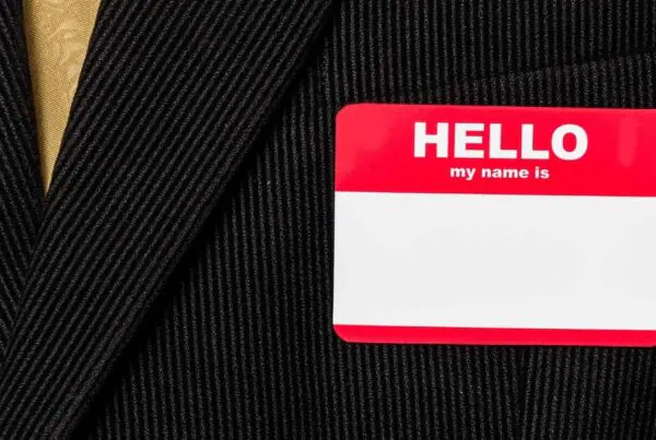A blank, red, and white nametag sticker on the breast of a black pinstripe suit with a golden tie.