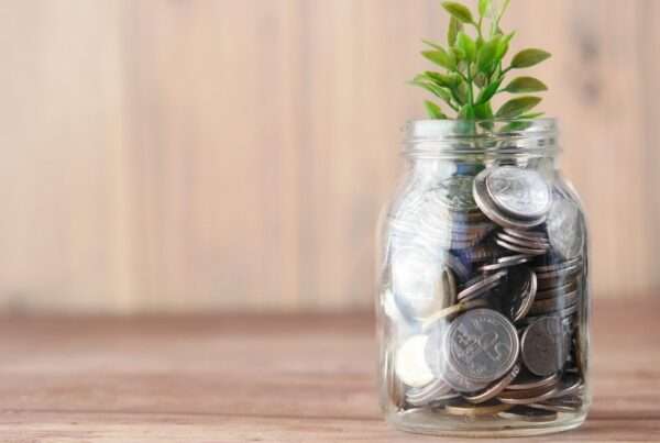 A mason jar of coins with a small plant growing out of the top against a wooden background.