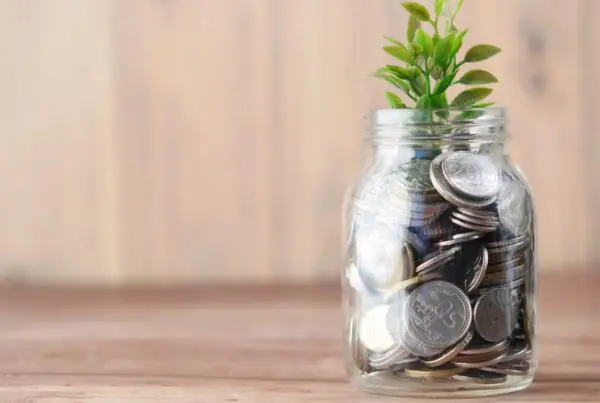 A mason jar of coins with a small plant growing out of the top against a wooden background.